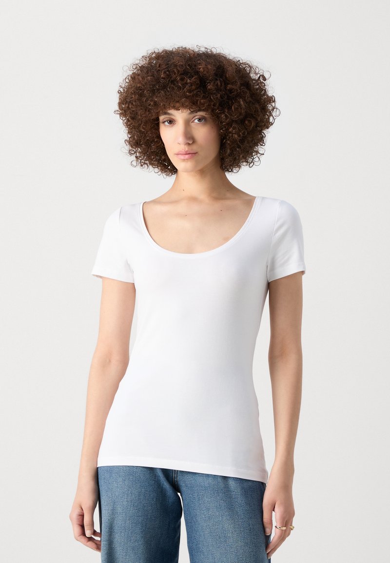 Chemise blanche à manches courtes avec un décolleté large en forme de bateau. Fabriquée à partir d'un matériau lisse et extensible. Associée à un jean bleu taille haute.