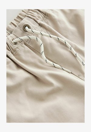 Beežist puuvillast lühikesed püksid, millel on kokku volditud elastne kummivöö, valge pael mustade aktsentidega ja metallist silmadega reguleerimiseks.