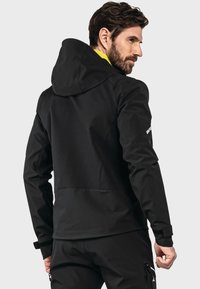 Schwarze Kapuzenjacke mit glatter Textur, figurnaher Passform und kontrastierender gelber Innenausstattung. Verfügt über minimalistische Akzente und eine mit Reißverschluss ausgestattete Tasche.