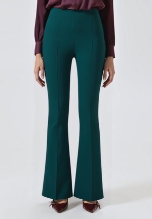 Pantaloni svasati in tessuto verde scuro, a vita alta, con cuciture verticali per un aspetto sartoriale, abbinati a scarpe bordeaux.