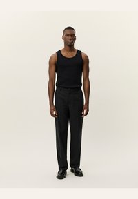 Black tank top and gray trousers worn by a model. The pants are tailored with a straight cut and subtle texture, complemented by black shoes.