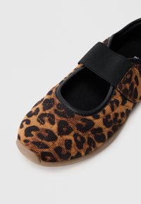 Leopard mønster Mary Jane sko i brunt og svart, med en kanvasoverdel og en svart justerbar stropp. Rund tå og fleksibel såle.