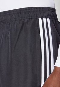 Schwarze sportliche Shorts aus leichtem Stoff mit strukturiertem Finish, versehen mit weißen vertikalen Streifen und einem elastischen Bund.