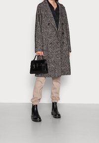 Cappotto oversize con motivo pied-de-poule in grigio e nero, design doppiopetto, abbinato a pantaloni jogger color cammello e stivaletti neri alla caviglia. Borsa nera inclusa.