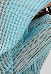 Top de punto de malla azul con diseño de calados, que presenta mangas largas y un corte relajado. La textura es ligera y transpirable.