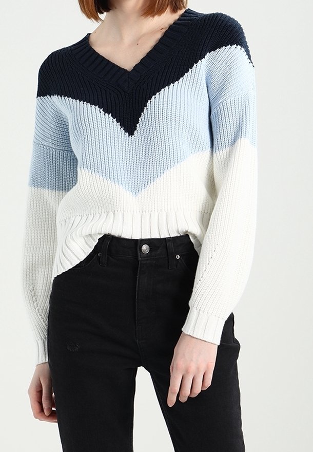 Pletený svetr s výstřihem do V, dlouhými rukávy a žebrovanou strukturou, zdobený chevronovým vzorem v námořnické modři, světle modré a bílé barvě. Nosit s černými džíny.