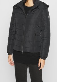 Chaqueta acolchada negra con cierre de cremallera, diseño acolchado, bolsillos laterales y capucha desmontable. Presenta puños de canalé y un acento de logo.