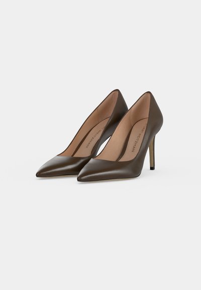 Paire d’escarpins marron foncé à bout pointu avec intérieur beige et talons aiguilles fins sur fond clair uni.