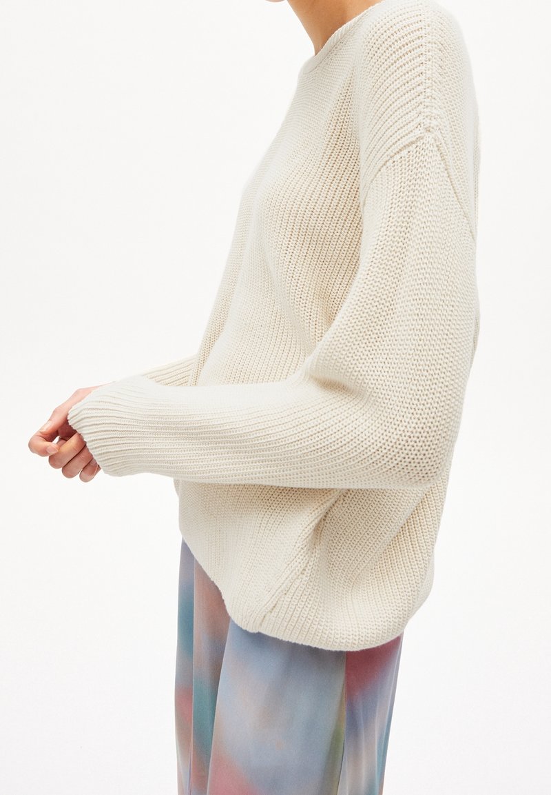 Pull en maille couleur crème avec une coupe ample, des manches larges et un motif texturé. Assorti à une jupe plissée tie-dye pastel.