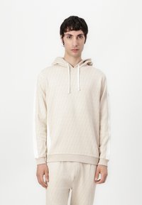 Felpa beige a motivi con tasca a marsupio, coulisse e accenti laterali bianchi. Tessuto morbido con polsini e orlo a coste. Pantaloni abbinati visibili.