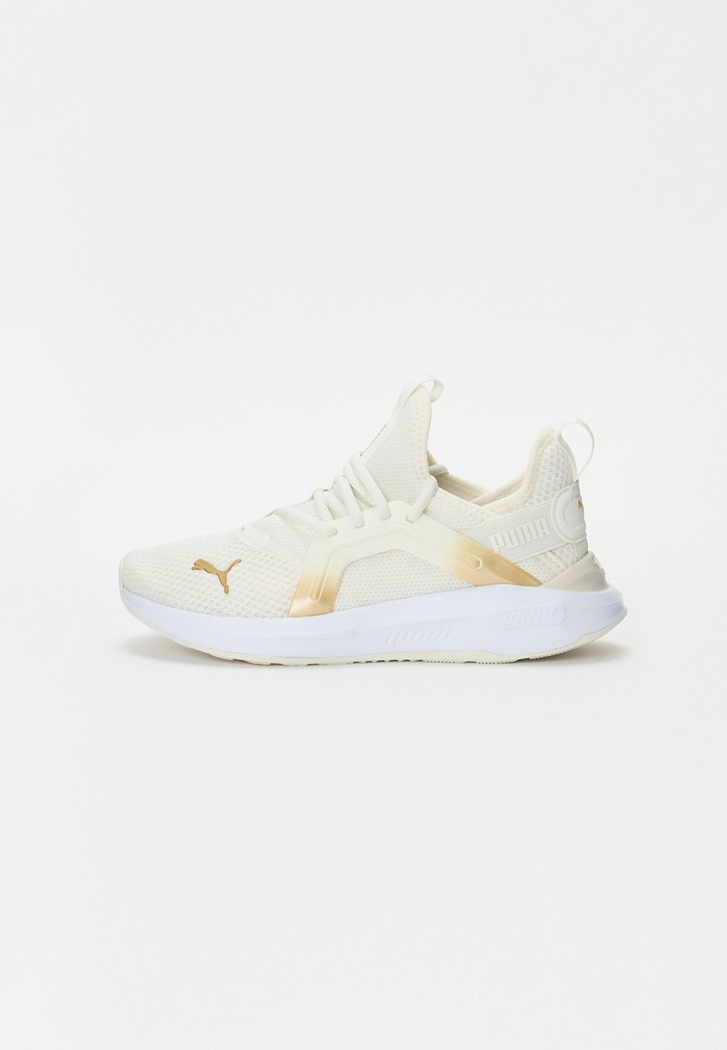 White athletic shoes with beige accents, mesh upper, elastic laces, and a textured sole. Features a gold logo on the side.