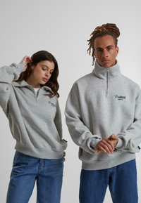 Sudadera con cremallera en gris, cuello alto, puños acanalados y corte relajado. Presenta un bordado de la marca en el pecho.