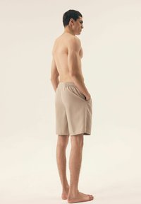 Beżowe kąpielówki z teksturowanym wzorem, z elastycznym pasem i bocznymi kieszeniami, prezentowane na modelu bez koszulki z tyłu.