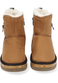 Bottes chelsea en daim marron avec un col en fausse fourrure, fermeture éclair latérale et semelle en caoutchouc présentant le nom de la marque sur le bord.