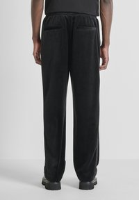 Zwarte, fluwelen broek met een ontspannen pasvorm, voorzien van een elastische tailleband en twee achterzakken. Eenvoudig ontwerp, zonder zichtbare patronen of accenten.