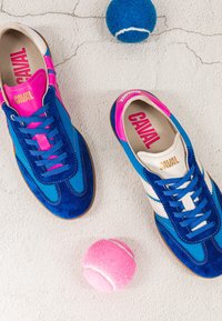 Paire de baskets Caval bleues et roses avec des lacets bleus, à côté d'une balle de tennis bleue et d'une rose sur une surface en béton clair fissurée.