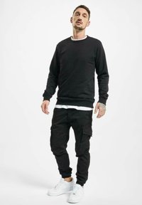 Čierna mikina s klasickým okrúhlym výstrihom, skombinovaná s čiernymi cargo nohavicami s bočnými vreckami. Biele tenisky so štýlovým dizajnom.