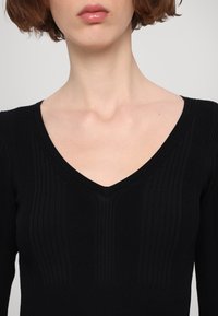 Maglietta nera a maniche lunghe con scollatura a V, caratterizzata da una texture a righe verticali e un design aderente. Tessuto morbido con una leggera lucentezza.
