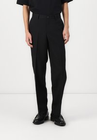Pantalon noir ajusté avec une coupe droite, présentant des plis à l'avant, des poches latérales et un tissu lisse. Fermeture à boutons à la taille.