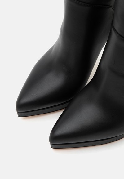 Bottes basses en cuir noir à bout pointu, finition lisse et semelle basse, vues en gros plan depuis un angle supérieur.