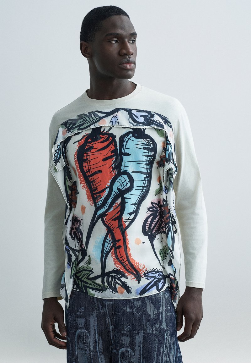 Πουκάμισο με μακριά μανίκια σε κρε μ απόχρωση με μεγάλο πολύχρωμο εκτυπωμένο σχέδιο με καρότα και φύλλα. Υφασμάτινες πινελιές με υφή στο μπροστινό μέρος.