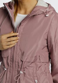 Różowa kurtka zapinana na zamek z przednim sznurkiem, biała, wyłożona polarem, kaptura oraz elastycznymi mankietami; subtelny połysk i gładka tekstura na całej powierzchni.