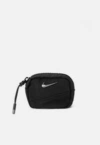Črna tkaninska torbica z teksturirano površino, opremljena s srebrnim logotipom Nike swoosh, z zadrgo in trpežnim vrvnim potegom.