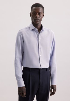 Herren Langarmhemd in Hellblau mit einem kleinen Karomuster, ausgestattet mit einem Button-Down-Kragen und weichem Stoff, kombiniert mit dunklen Hosen.