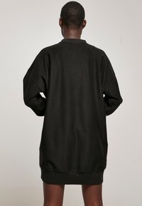 Abito nero oversize a coste con colletto rotondo, spalle scese e vestibilità morbida, caratterizzato da una texture morbida e lunghezza fino a metà coscia.