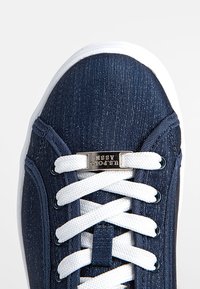 Baskets bleu marine avec lacets blancs et semelle blanche, avec une étiquette métallique sur les lacets avec la marque "U.S. Polo Assn.".
