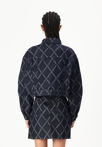 Geknipt spijkerjasje en rok in donkerblauw met een gemusterd ontwerp. Voorzien van grote zakken en een klassieke kraag.