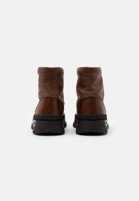 Bottines en cuir marron à finition mate, à bout rond, avec une semelle noire robuste et un minimum de couture sur le dessus.