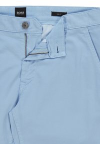 Světle modré slim-fit kalhoty s hladkou texturou, které mají zipový přední díl, zapínání na knoflík a propracované švy. Značka BOSS viditelná.