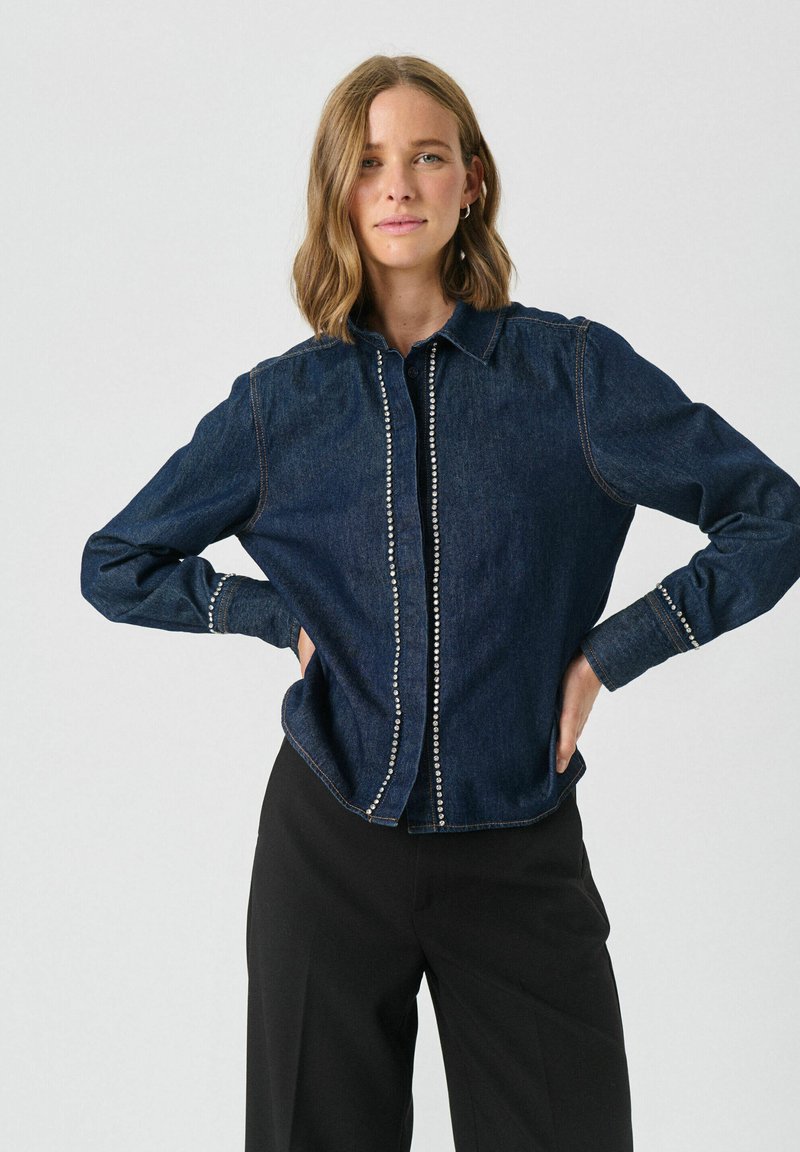 Donkerdenim shirt met een kraag, voorzien van een rij decoratieve studs aan de voorkant en op de manchetten, lange mouwen en een relaxte pasvorm.