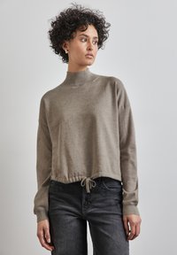 Maglione corto di colore marrone chiaro con collo alto e orlo con cordoncino. Texture morbida, maniche lunghe e polsini a coste si abbinano bene a jeans neri casual.