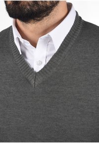 Grau gestrickter Pullover mit V-Ausschnitt, kombiniert mit einem weißen Hemd mit Kragen. Der Stoff wirkt glatt und strukturiert mit dezenten Nähten.