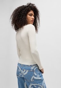 Ribbet, off-white langermet topp kombinert med lyseblå jeans med stort grafisk design og baklommer. Glatt tekstur, tettsittende form.