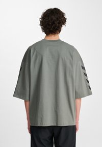 Olijfgroene oversized t-shirt met korte mouwen. Heeft zwarte diagonale strepen op de mouwen en een ronde hals. Soepele katoentextuur.