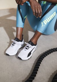 White athletic shoes with black accents and gray detailing, featuring a mesh upper and laces, paired with blue leggings with black and neon highlights.