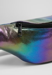 Iridescent hoftepose med en tekstureret overflade, der har en sort lynlås og en buet form. Farverne skifter fra lilla til blå-grøn.