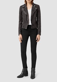 Giacca da motociclista in pelle nera con spalle trapuntate, zip frontale e dettagli in metallo argentato, abbinata a jeans skinny neri e stivaletti.