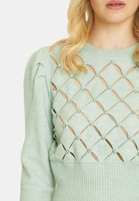 Maglione verde chiaro con intagli a forma di diamante, decorato con strass, vita in tessuto a coste e maniche a palloncino per un aspetto strutturato.