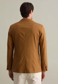 Blazer di cotone marrone con revers classico, chiusura con un solo bottone e tasche laterali, con un design posteriore pulito e una silhouette aderente.