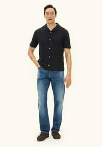 Czarna koszula na krótki rękaw z guzikami i teksturowanym wzorem, zestawiona z jasnoniebieskimi dżinsami i brązowymi butami na sznurowadła.