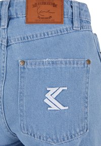 Svetlomodré denimové nohavice s koženou nášivkou a vyšívaným logom na zadnej vrecku. Obsahujú medené nitové detaily a viditeľné švy.