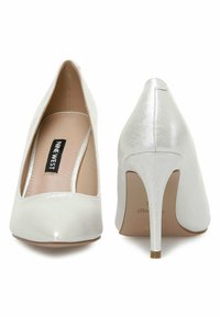 Valged kõrged kontsad läikiva viimistlusega, terava nina ja saleda stilettokontsaga. Siseosas on brändi logo kujundus.