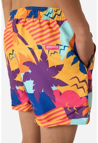 Farverige badeshorts med et tropisk design med palmer, zigzag-mønstre og en blanding af orange, lilla, blå og pink farver.