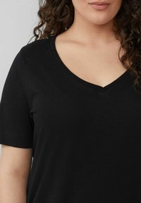 Schwarzes V-Ausschnitt T-Shirt aus weichem Stoff, mit kurzen Ärmeln und lockerem Schnitt. Der Ausschnitt hat einen dezenten Saum für zusätzliche Details.