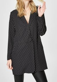 Schwarze Bluse mit Polka-Dots, V-Ausschnitt und langen Ärmeln. Verfügt über eine Knopfverschluss und einen lockeren Schnitt, hergestellt aus glattem Stoff.