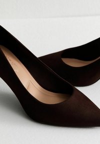 Décolleté neri in suede con punta a punta e design dei lati ritagliato. Texture liscia e soletta beige completano l'esterno scuro.